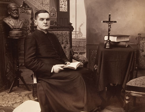 Father Michael J. McGivney seated in a rectory setting circa 1880