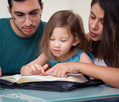 Mother and father helping their daughter in reading the bible