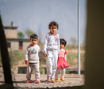 Three refugee children facing a camera 