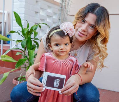 A young mother holds her ultrasound film with her daughter in her arms