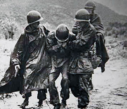 Father Kapaun (right) and Capt. Jerome A. Dolan, a medical officer with the 8th Cavalry Regiment, help an exhausted soldier off the battlefield.