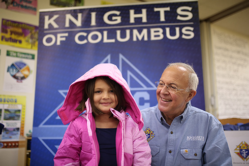 Supreme Knight facing the camera with a child who received a coat from Knights of Columbus.