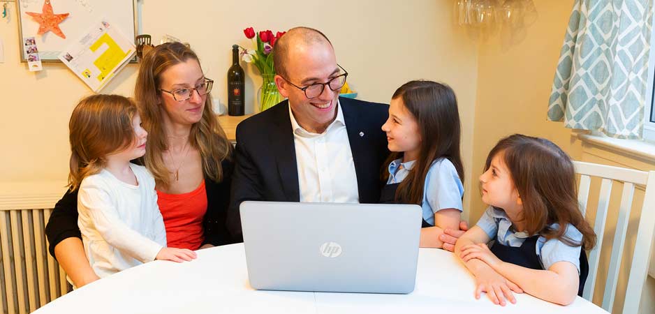 Parents smiling with three young daughters as they gather around a computer