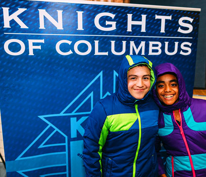 Kids smile while wearing winter coats donated by the Knights of Columbus